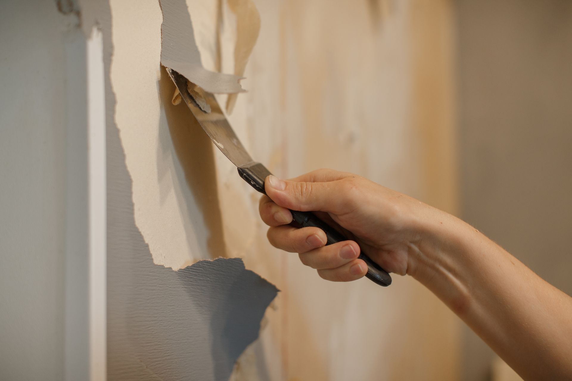 Hand scraping peeling paint from a wall with a putty knife