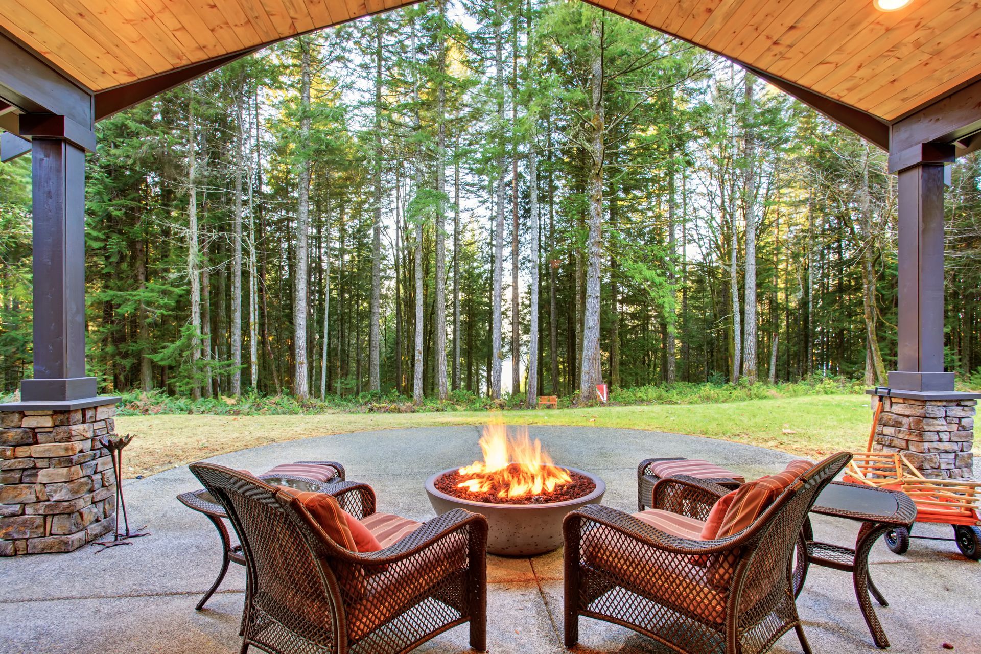 Covered patio with wicker chairs around a fire pit, overlooking a forest of tall trees.