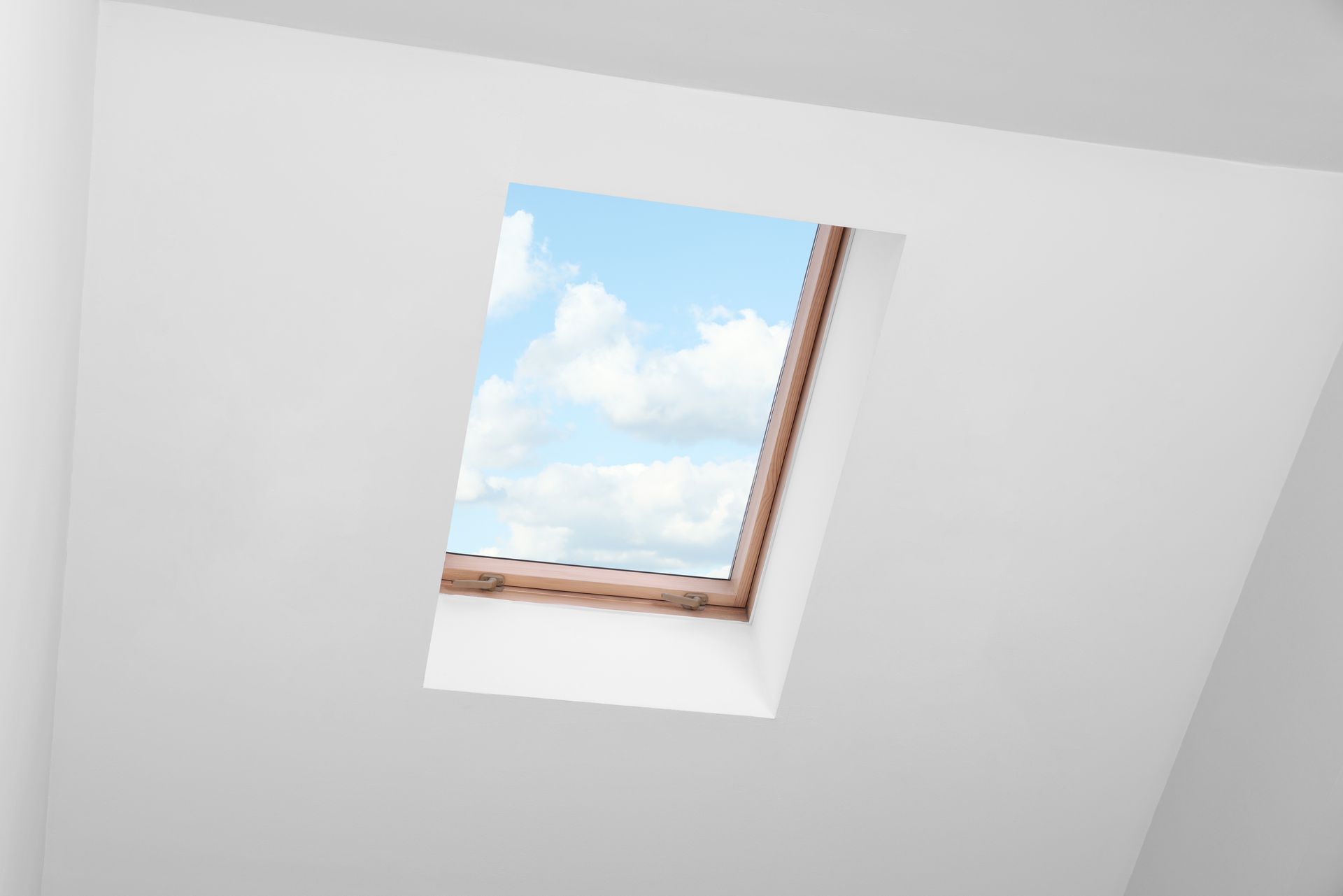 Tilted skylight window with blue sky and clouds against a white ceiling