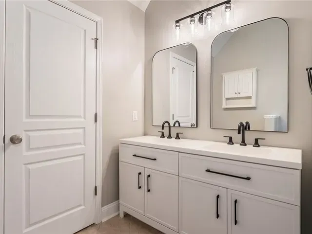 Modern white bathroom vanity with two mirrors, black faucets, and a closed door