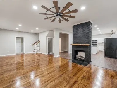 Bright open living room with hardwood floors, black fireplace, ceiling fan, and adjoining kitchen area