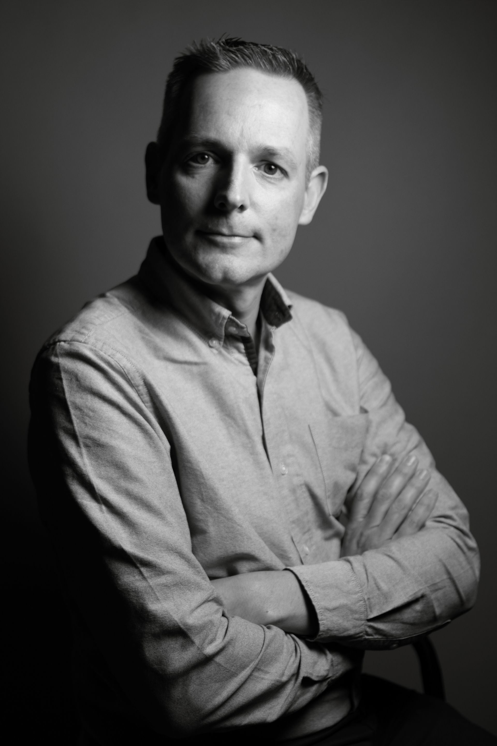 Peter Curtis in a button-down shirt with arms crossed, looking at the camera. Black and white, studio setting.