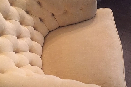 Beige tufted upholstered sofa with a rounded arm and soft cushions