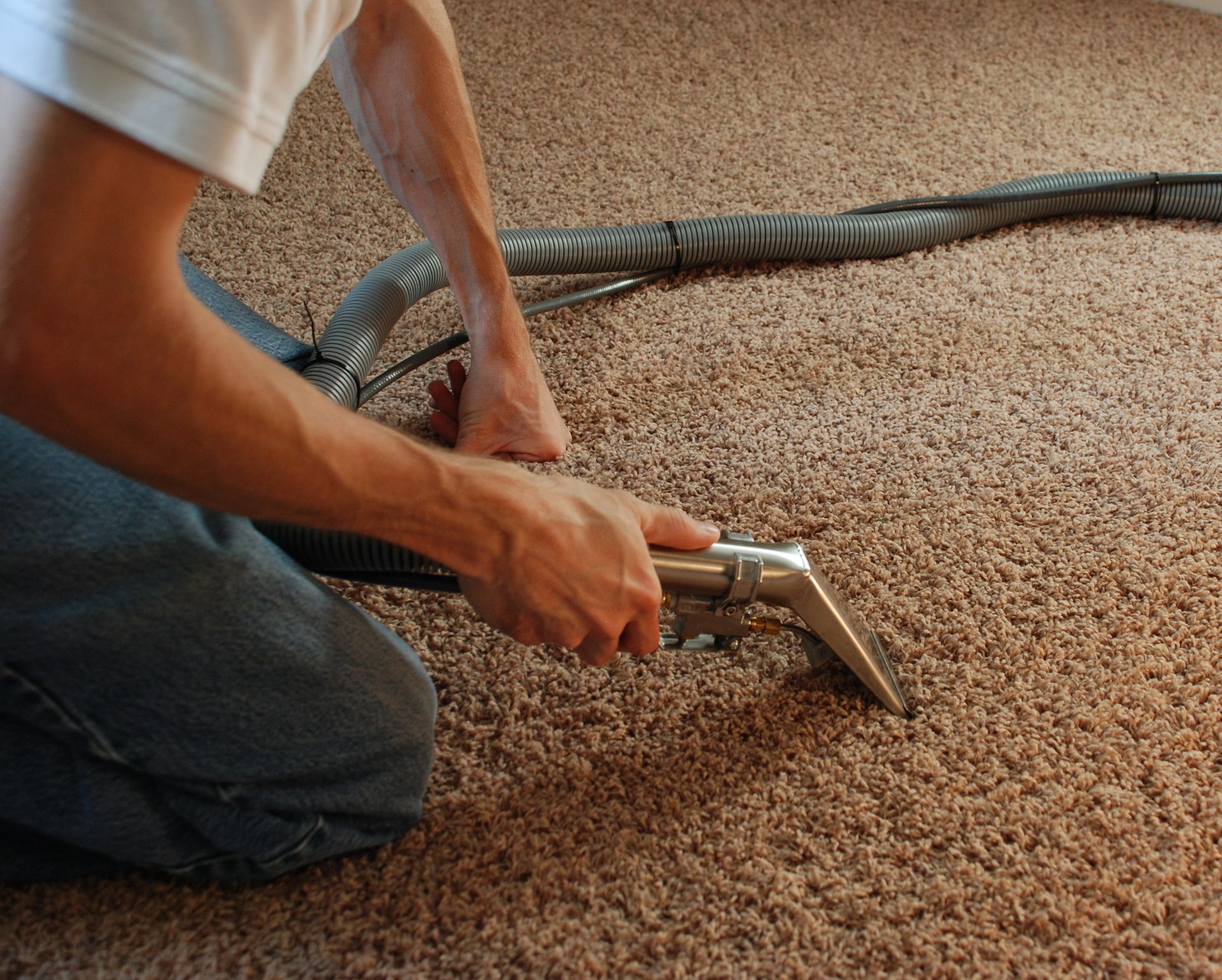 Person kneeling and smoothing carpet with a metal tool on the floor