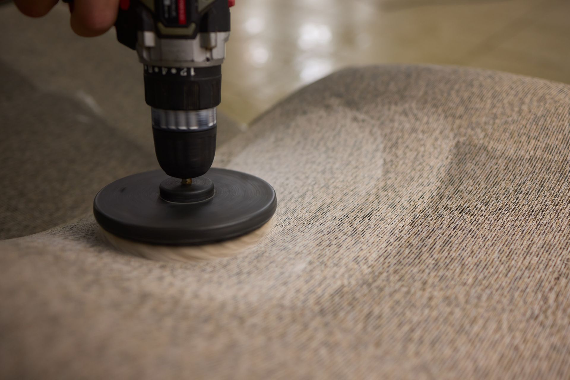 Cordless drill with polishing pad buffing a beige carpet or upholstered surface