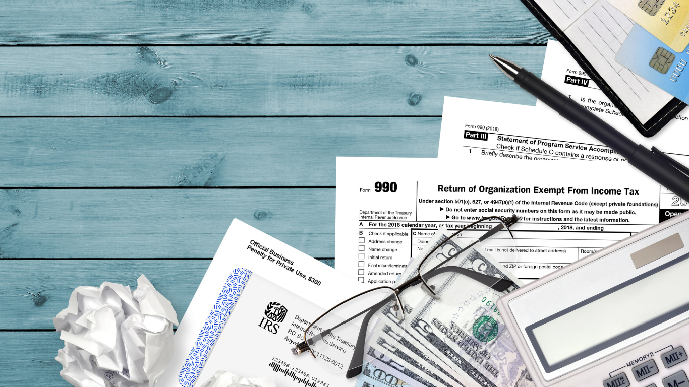 A bunch of papers including an IRS 990 form and a calculator on a wooden table