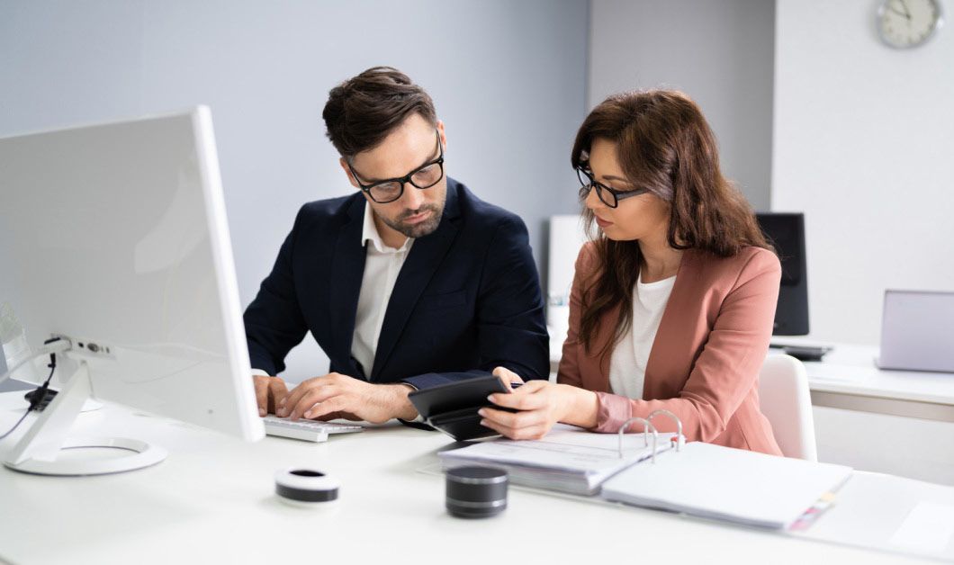 A man and a woman are sitting at a desk in front of a computer. - boi obligation
