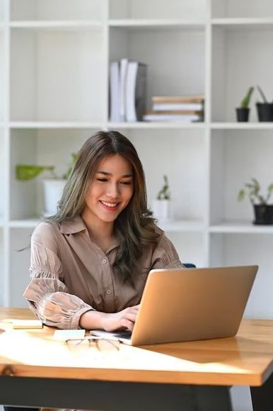 A woman is sitting at a desk using a laptop computer.