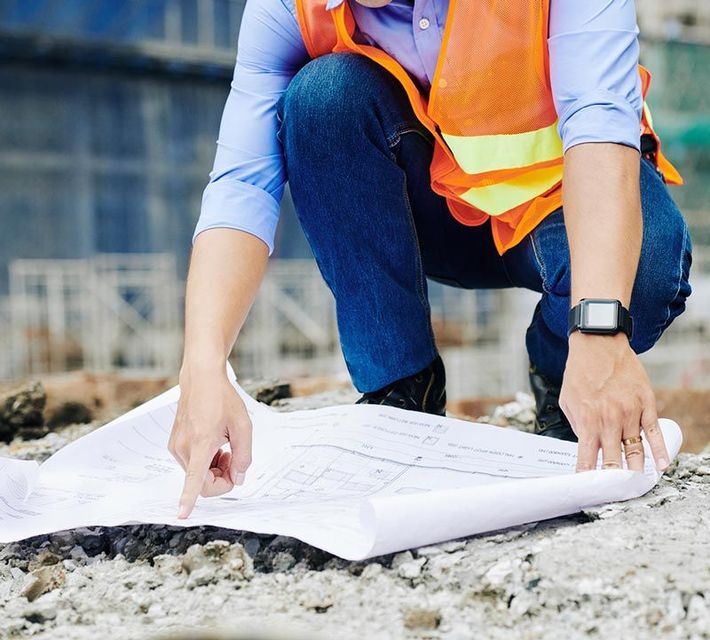 A construction worker is kneeling down looking at a blueprint.
