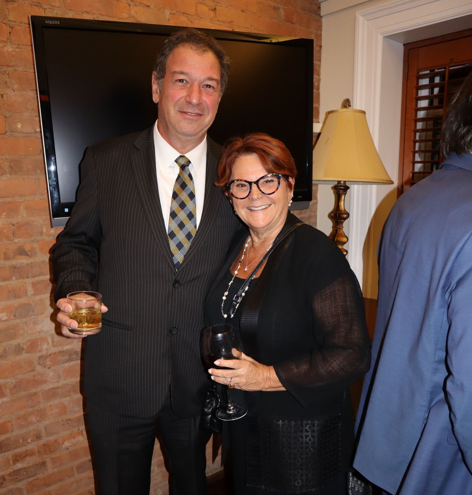 A man in a suit and tie stands next to a woman in glasses