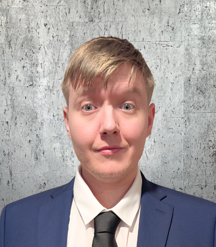 A man in a suit and tie stands in front of a concrete wall