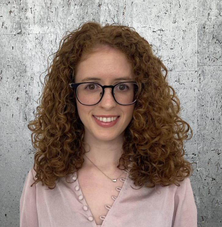 A woman with curly hair wearing glasses and a pink shirt