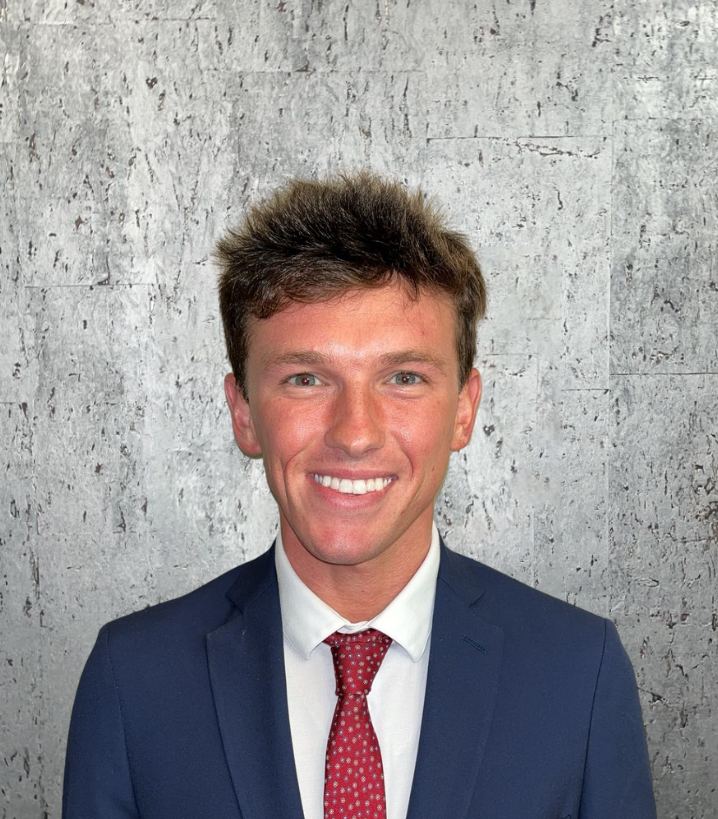 A man in a suit and tie is smiling in front of a concrete wall