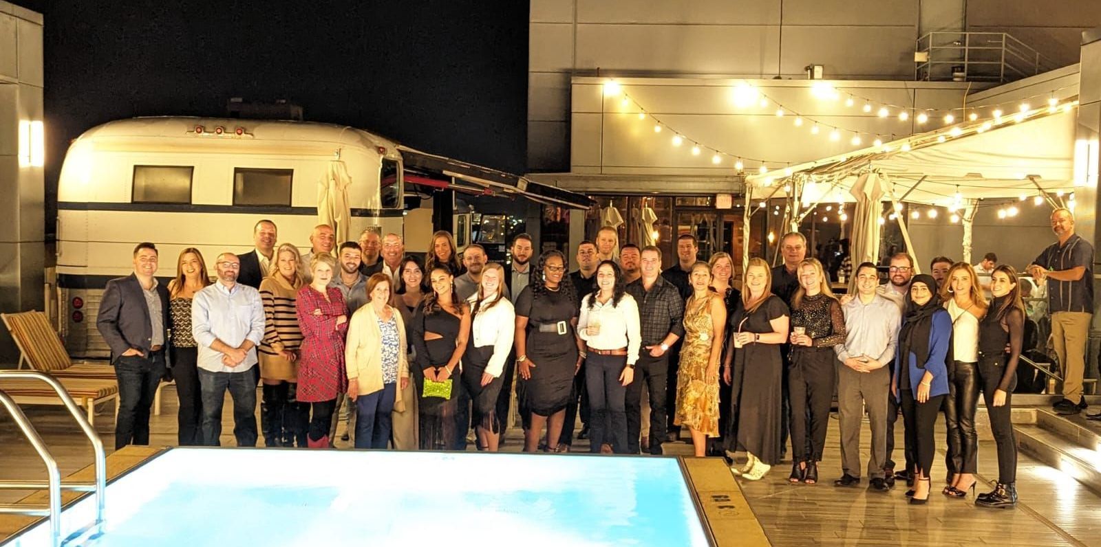A large group of people are standing next to a swimming pool at night.