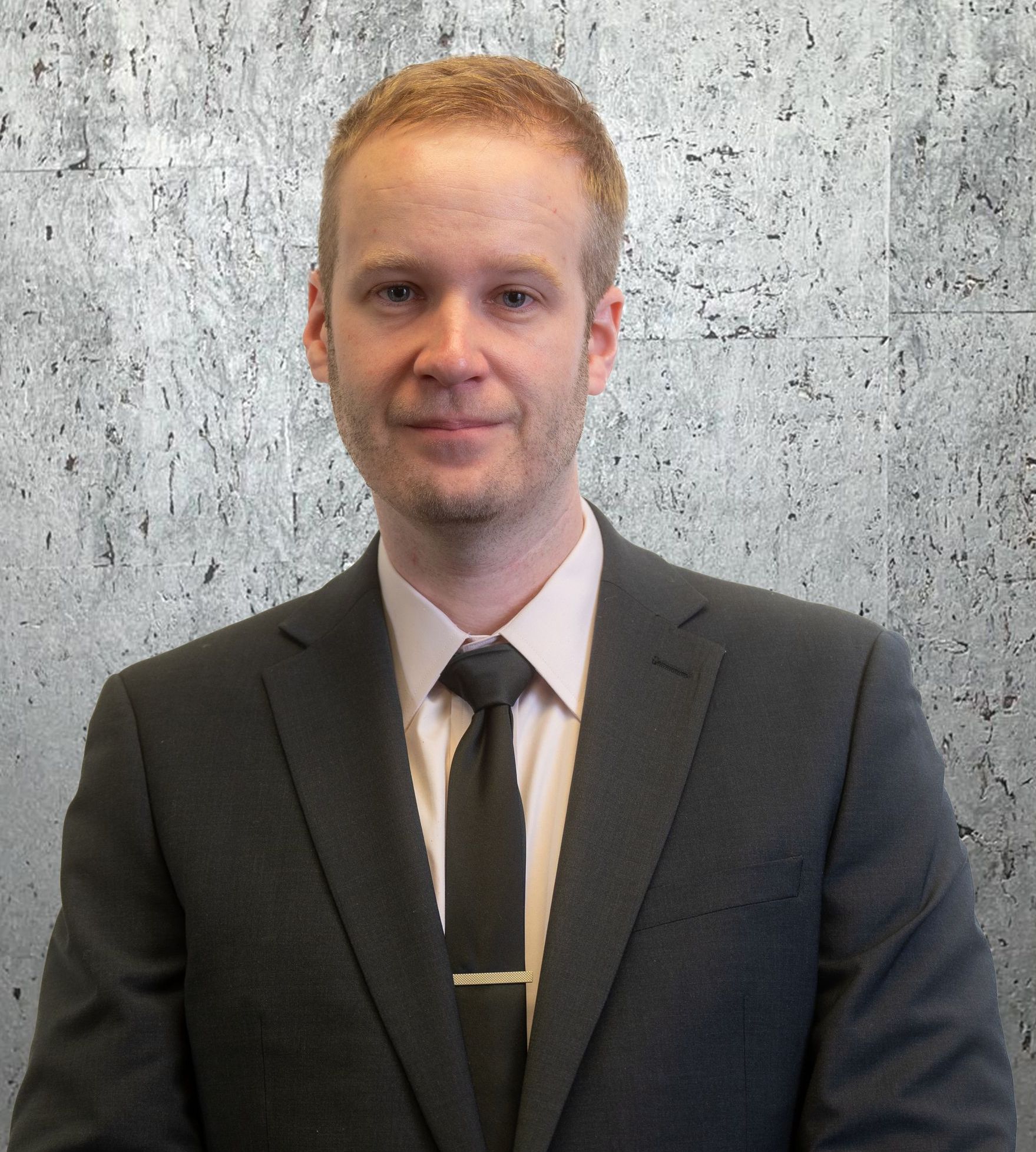 A man in a suit and tie is standing in front of a concrete wall.