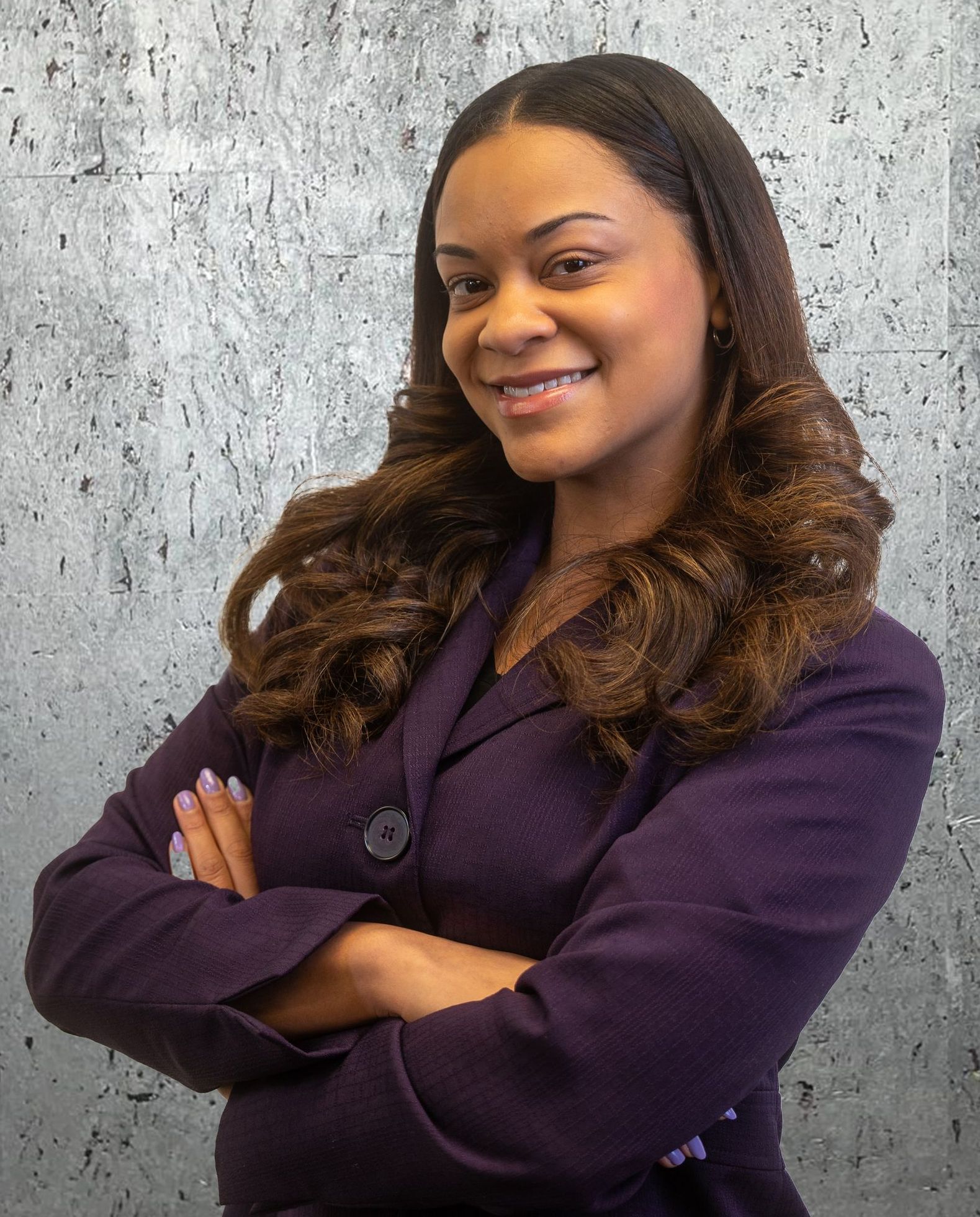 A woman in a purple suit is posing for a picture with her arms crossed.