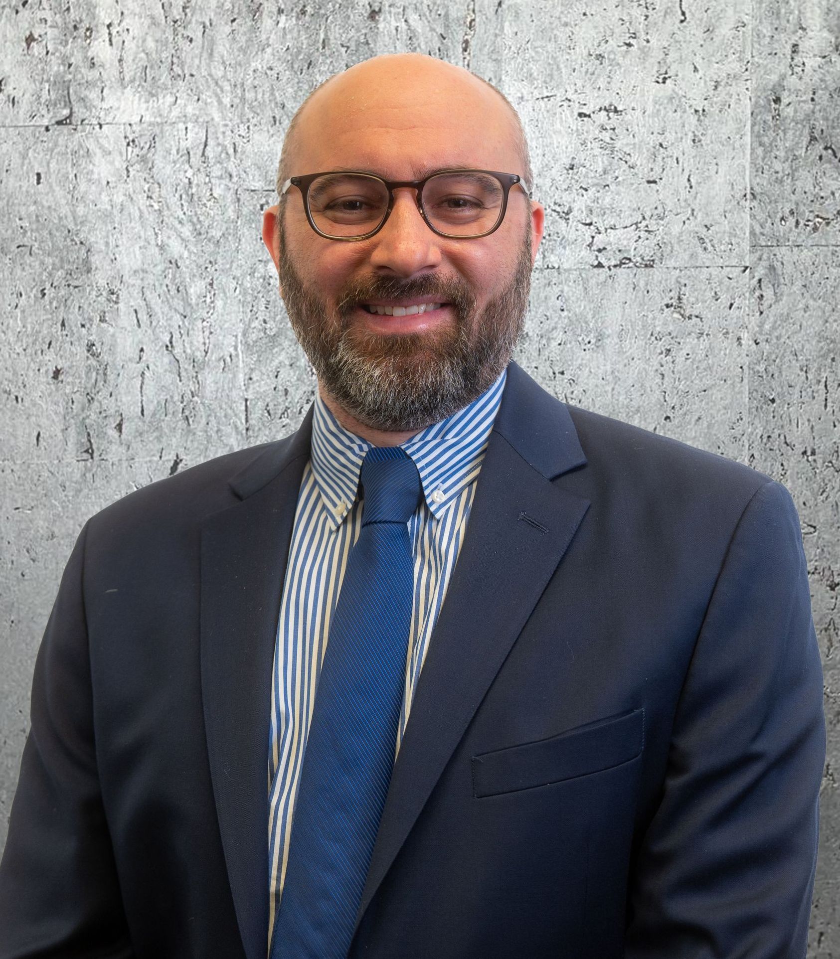 A man with a beard and glasses is wearing a suit and tie.