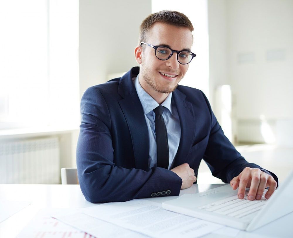 A man in a suit and tie is sitting at a desk using a laptop