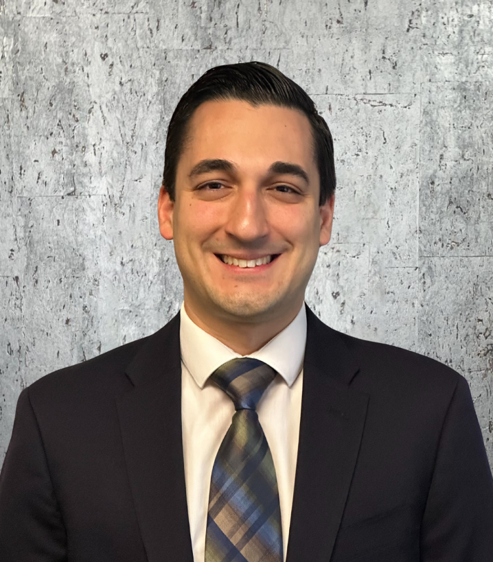 A man in a suit and tie is smiling in front of a concrete wall.