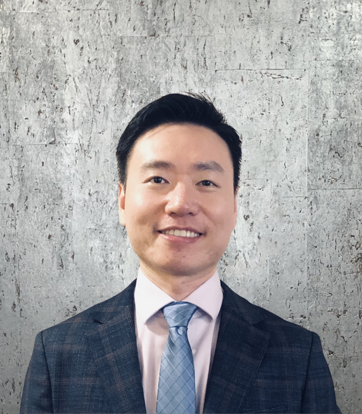 A man in a suit and tie is smiling in front of a concrete wall