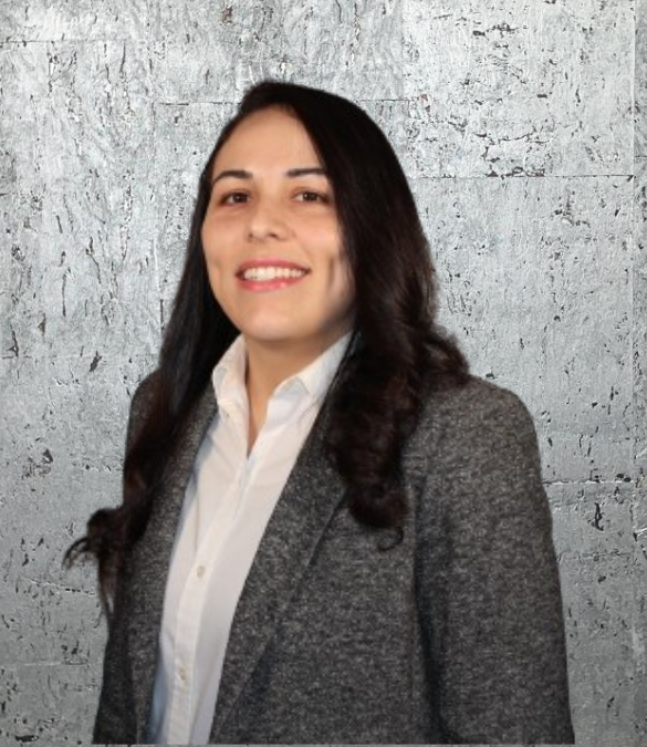 A woman in a suit and white shirt is smiling in front of a brick wall.