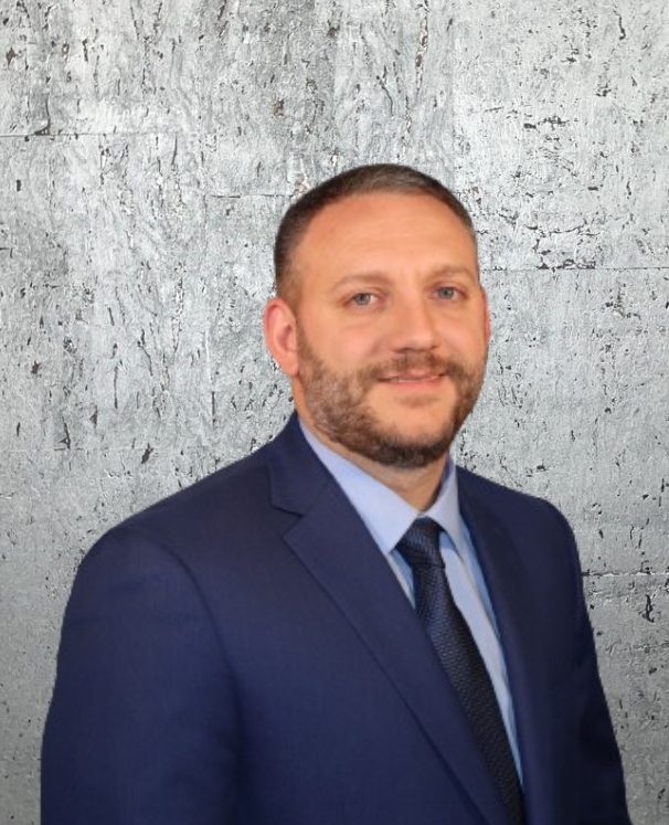 A man in a suit and tie is standing in front of a gray wall.