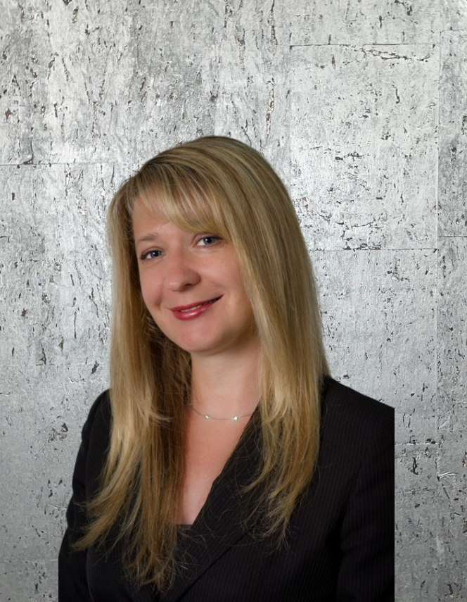 A woman in a black suit is smiling in front of a concrete wall.