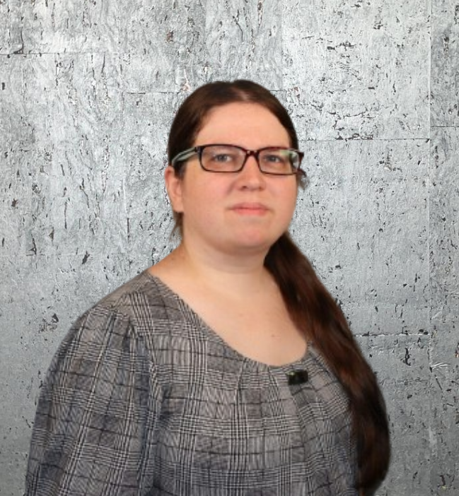 A woman wearing glasses and a plaid shirt is standing in front of a wall.