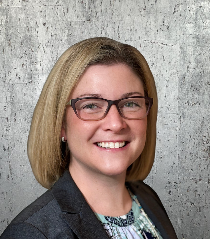 A woman wearing glasses and a jacket is smiling for the camera.