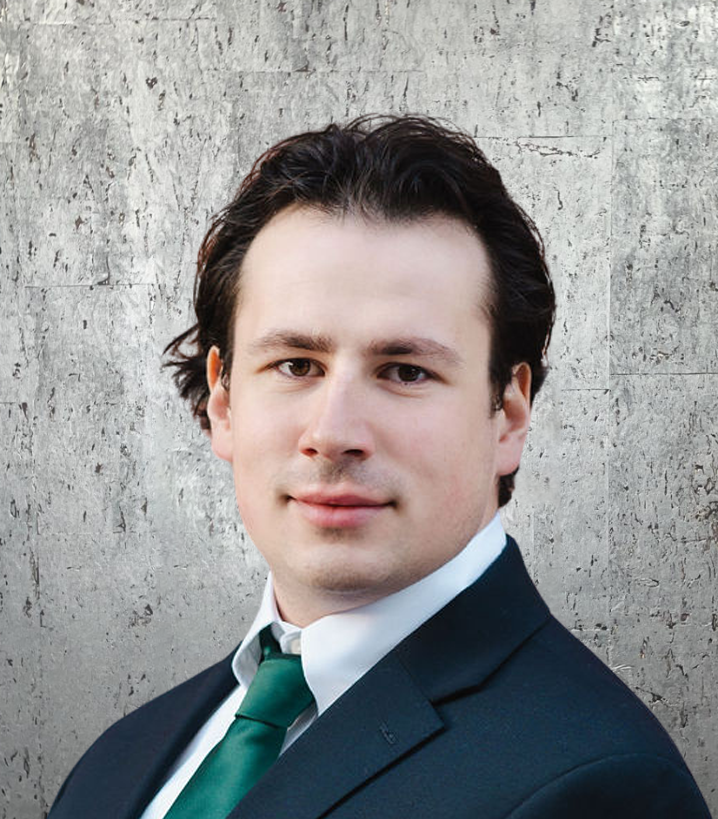 A man in a suit and tie stands in front of a concrete wall
