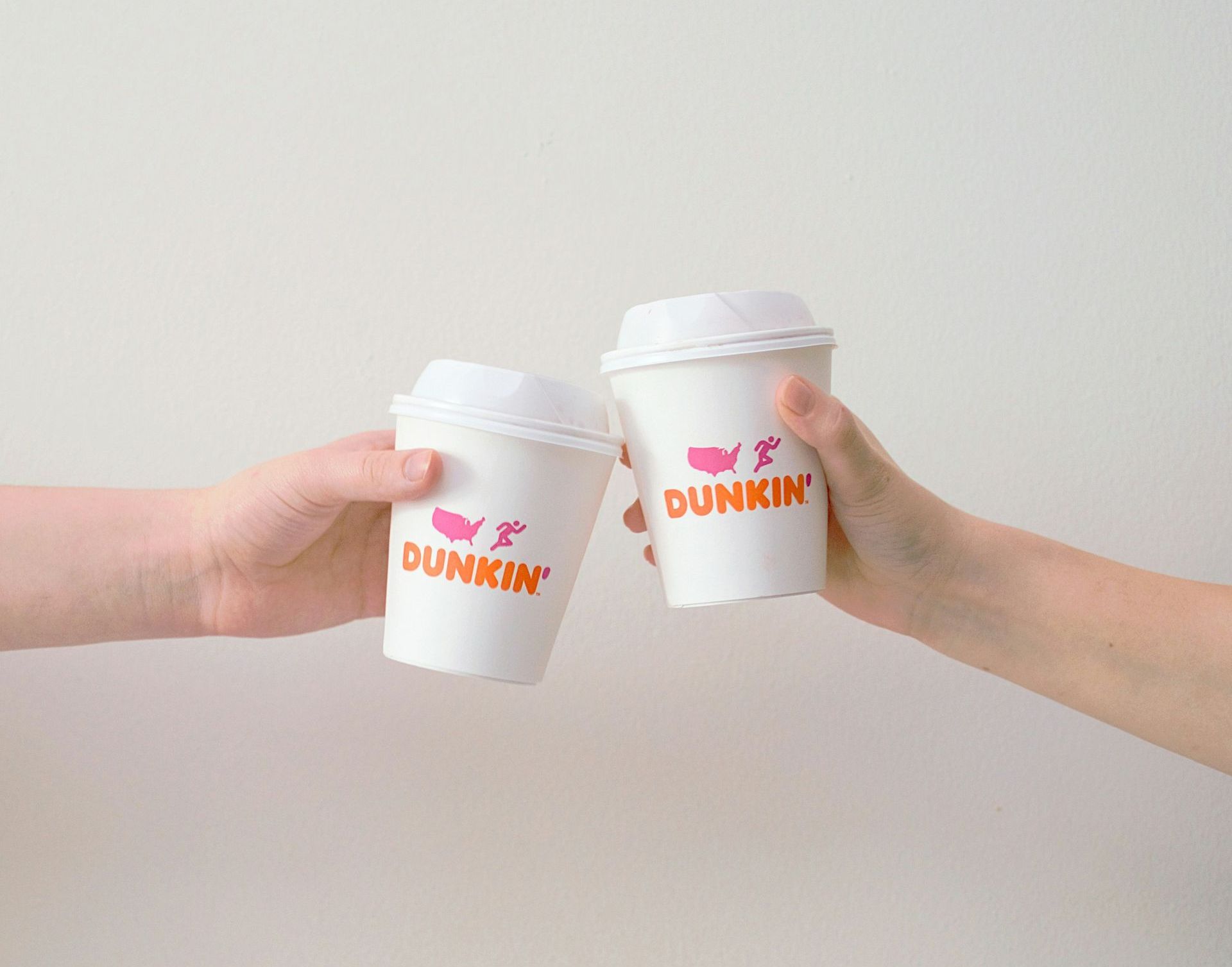 Two people are toasting with two cups of dunkin ' donuts.