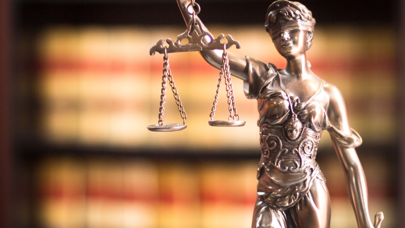 Statue of Lady Justice holding scales, library shelves in the background.