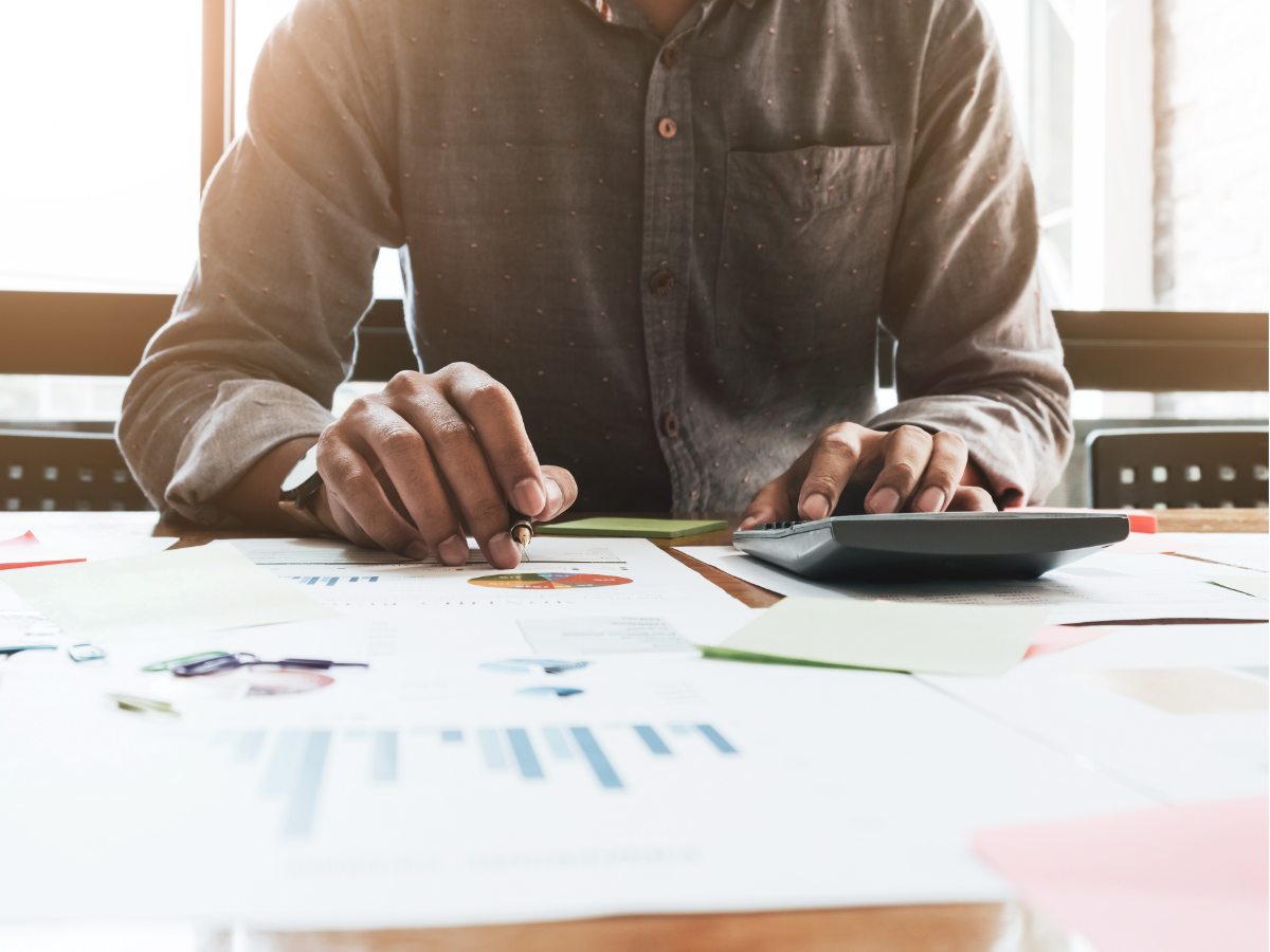Person using a calculator, looking at charts and papers on a desk.