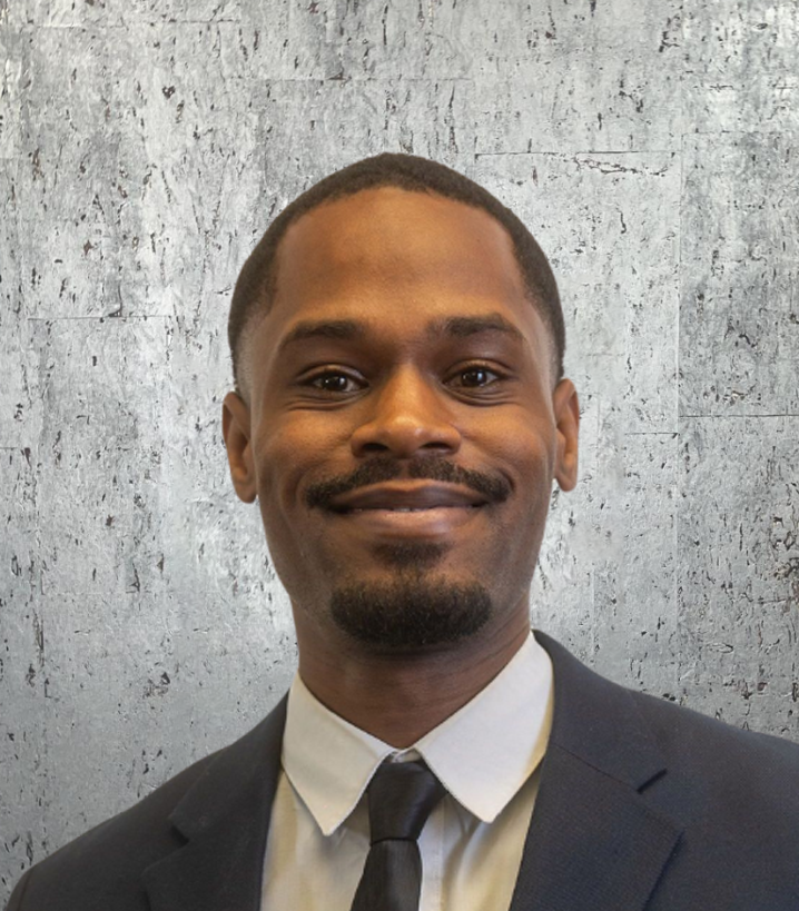 Man in a suit smiles at the camera, against a textured gray background.