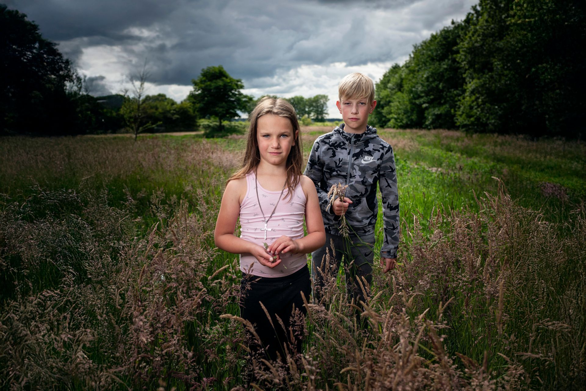 Twee kinderen staan ​​in een veld met hoog gras onder een bewolkte hemel.