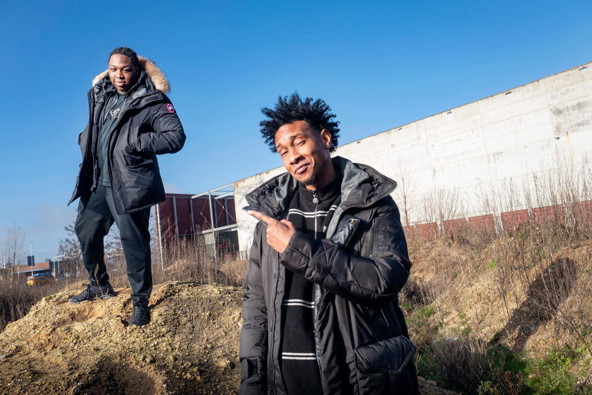 Twee mannen in winterjassen staan ​​buiten. De ene wijst, de andere kijkt toe. Blauwe lucht. 