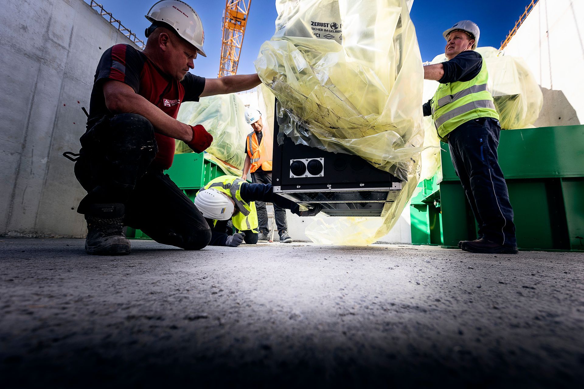 Bouwvakkers plaatsen apparatuur op een betonnen ondergrond, met een kraan.