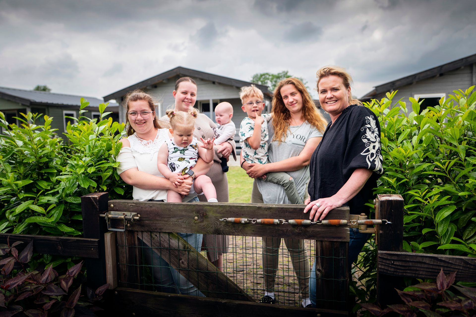 Een groep moeders met jonge kinderen voor een houten tuinhek, met een huis op de achtergrond.