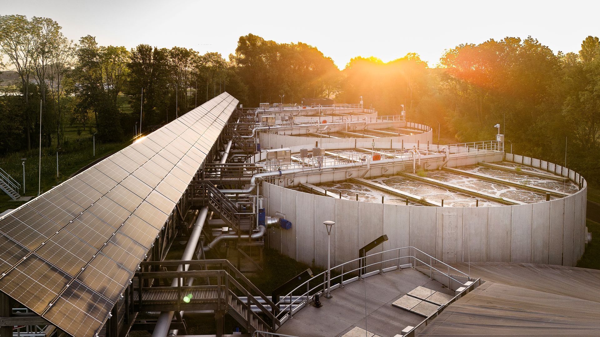 Zonnepanelen en waterzuiveringstanks baden in opkomende zonlicht.