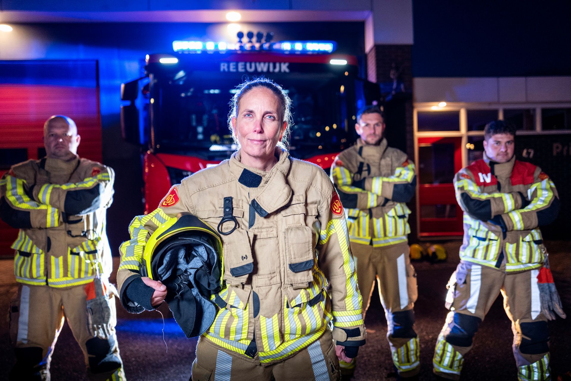 Brandweerlieden voor een brandweerwagen Ze dragen beschermende kleding en poseren.