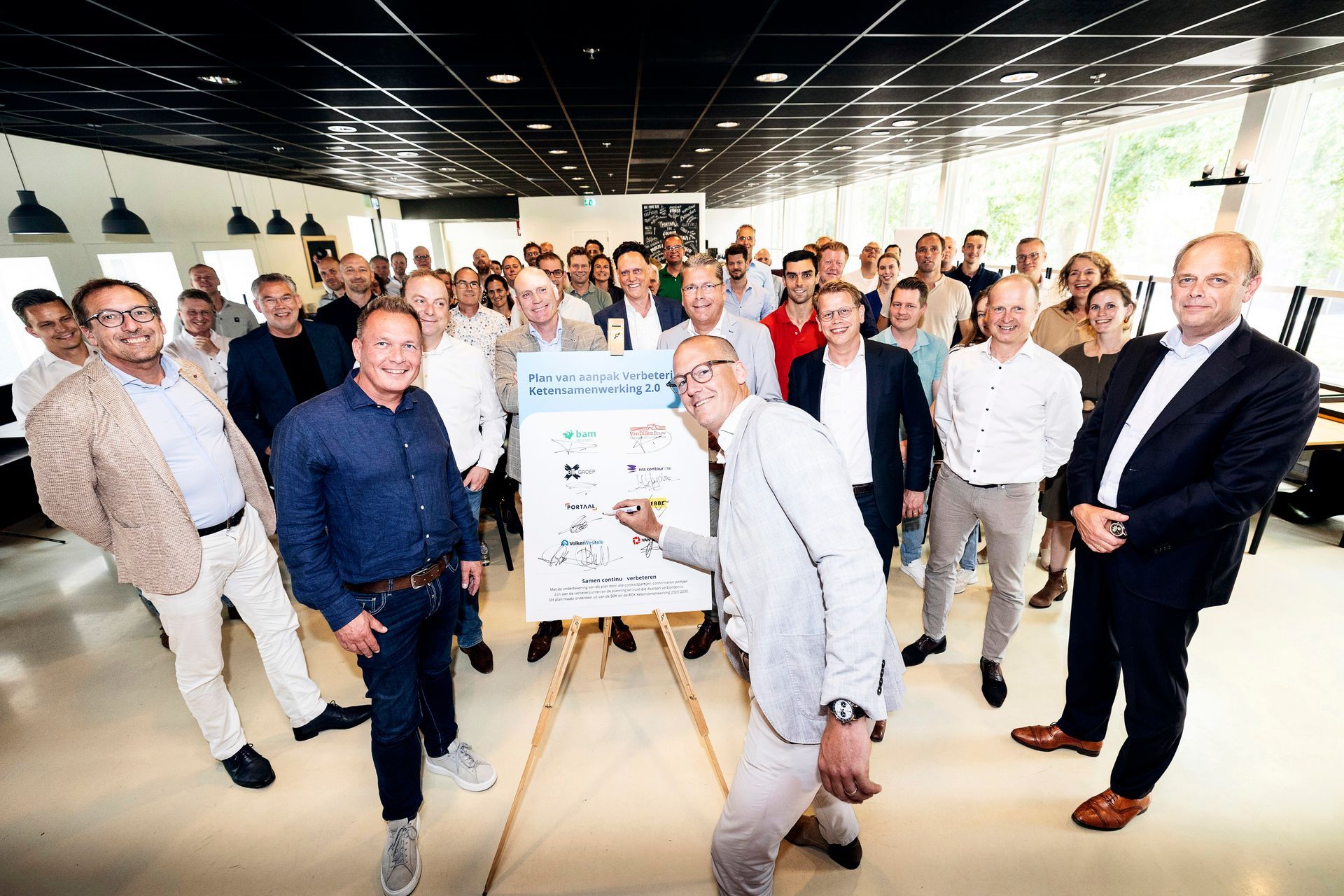Een grote groep mensen staat binnen rond een ondertekening op een presentatiebord. 