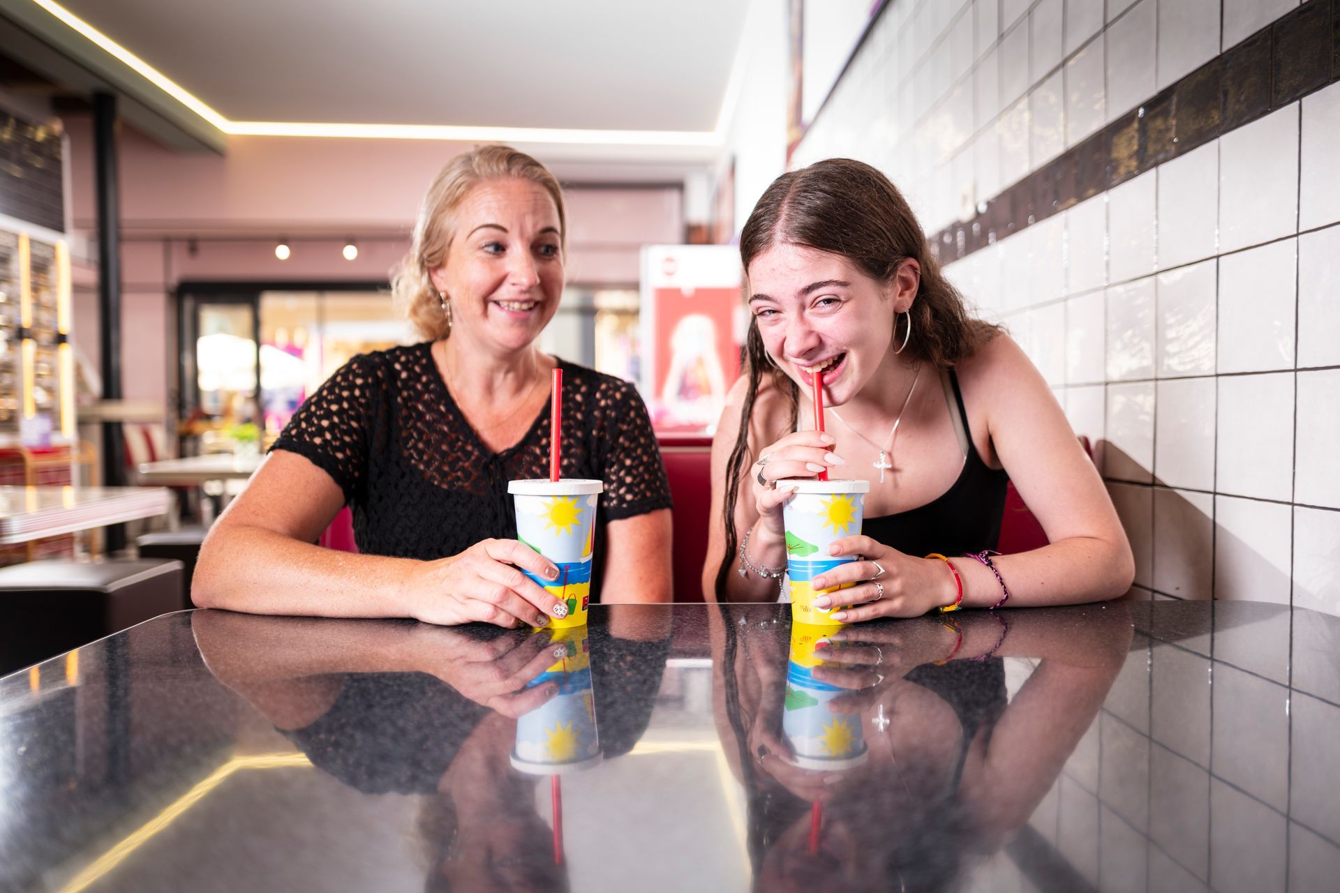 Vrouw en meisje in een restaurant aan een tafel, met bekers met rietjes; meisje lacht.