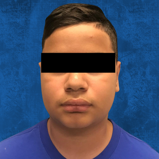 A person wearing a blue shirt against a blue background, with their eyes obscured by a black bar.