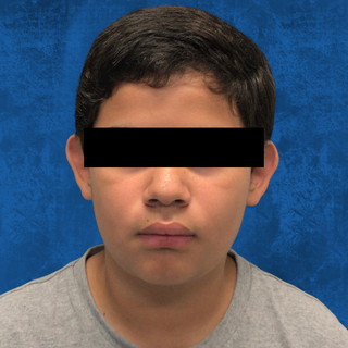 A person with a neutral expression faces forward against a solid blue background, with a black bar over their eyes.
