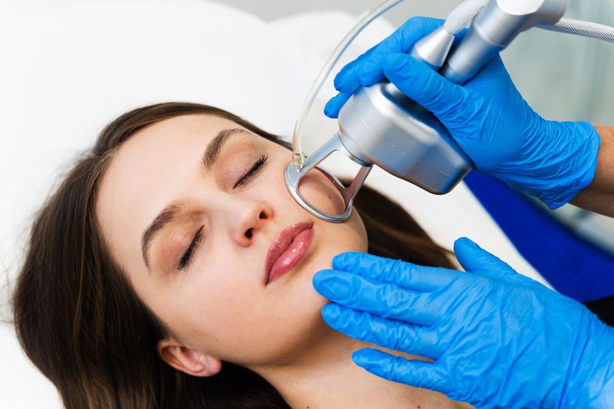 Cosmetologist using a handheld device on a woman's face during a skincare treatment