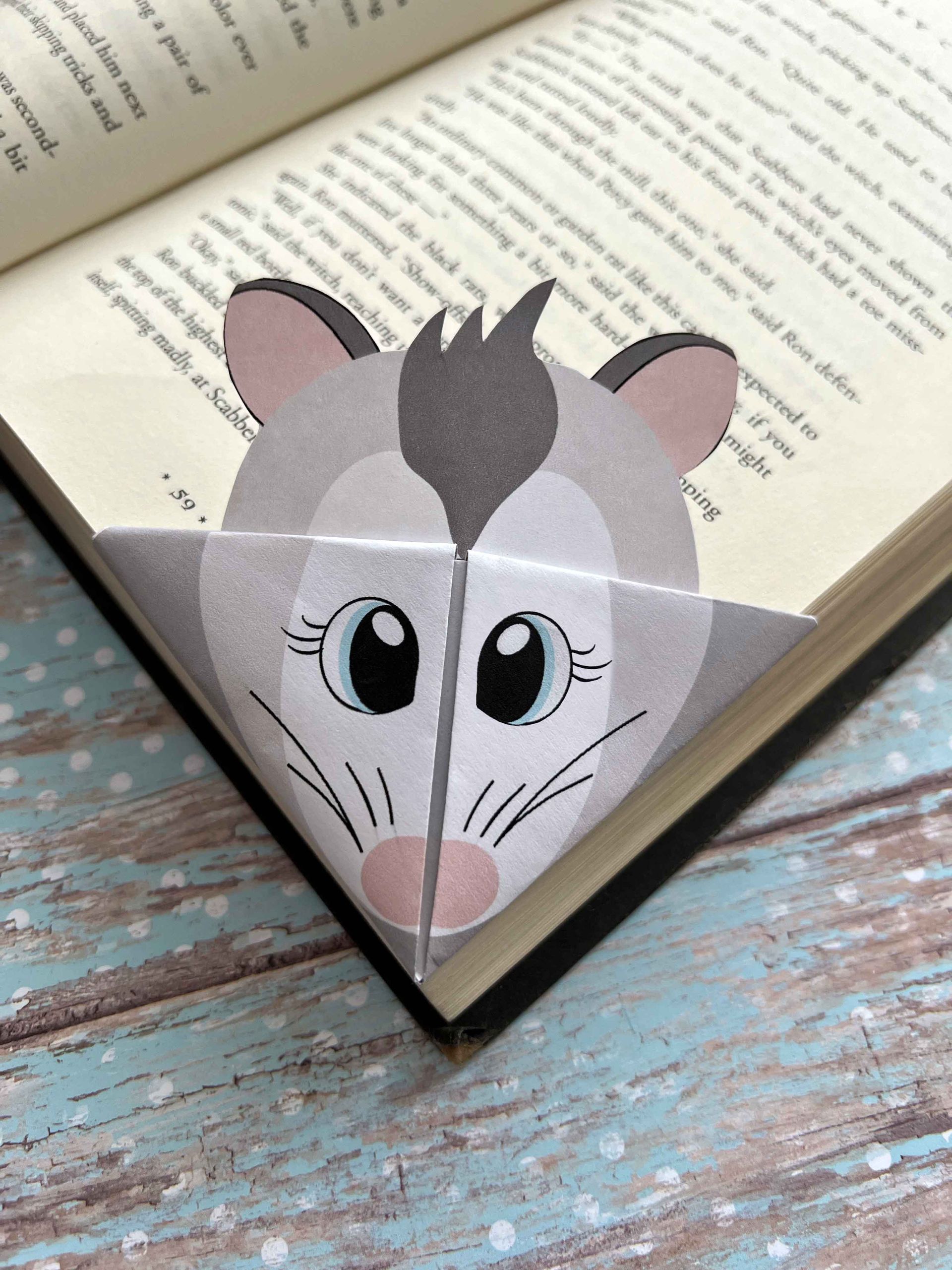 A handmade opossum corner bookmark inserted into an open book.