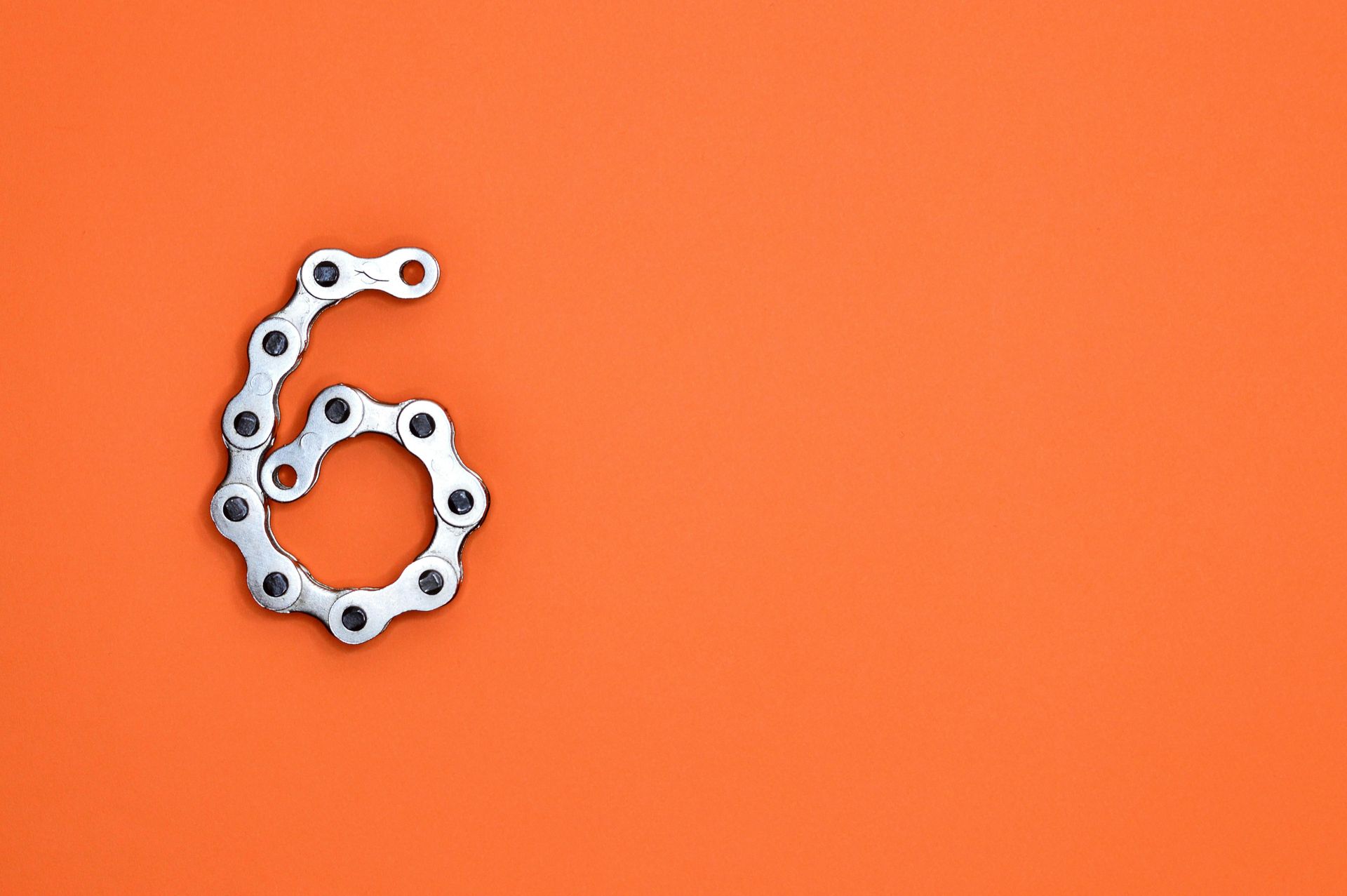 Number 6 formed from a bicycle chain, on a solid orange background.