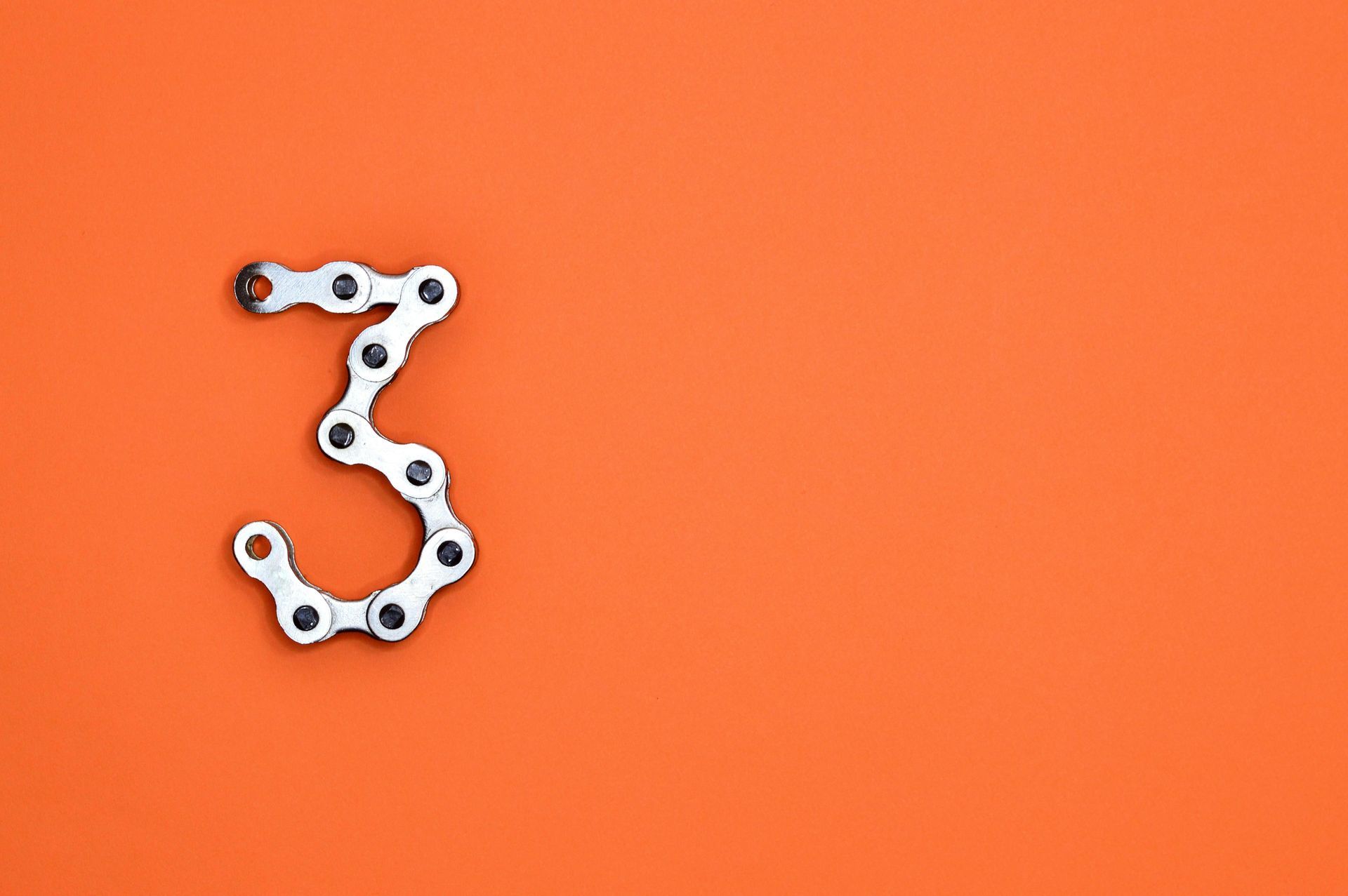 Number 3 formed with a silver bicycle chain on an orange background.