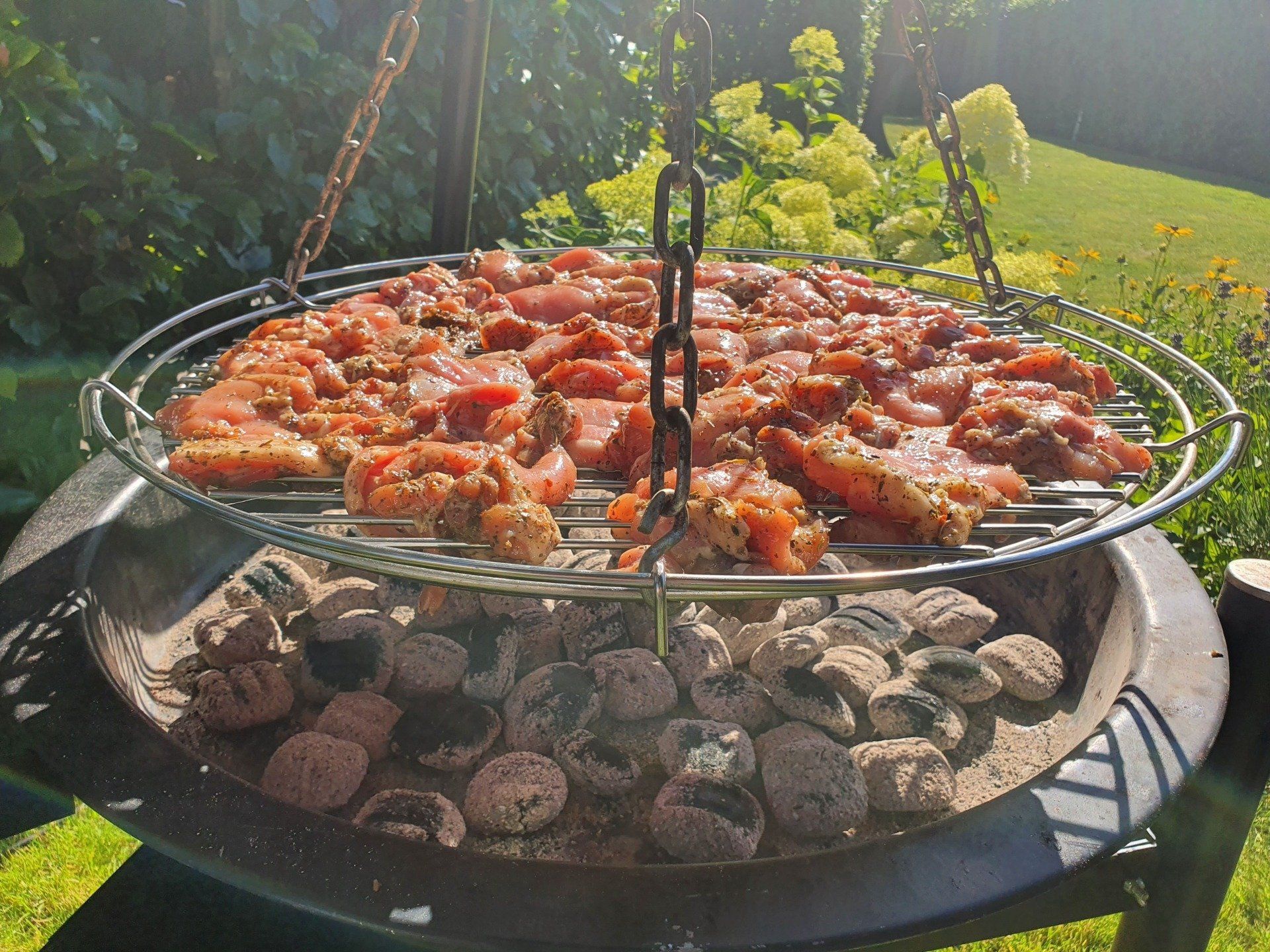Vlees grillen op een ronde driepoot barbecue met hete kolen.