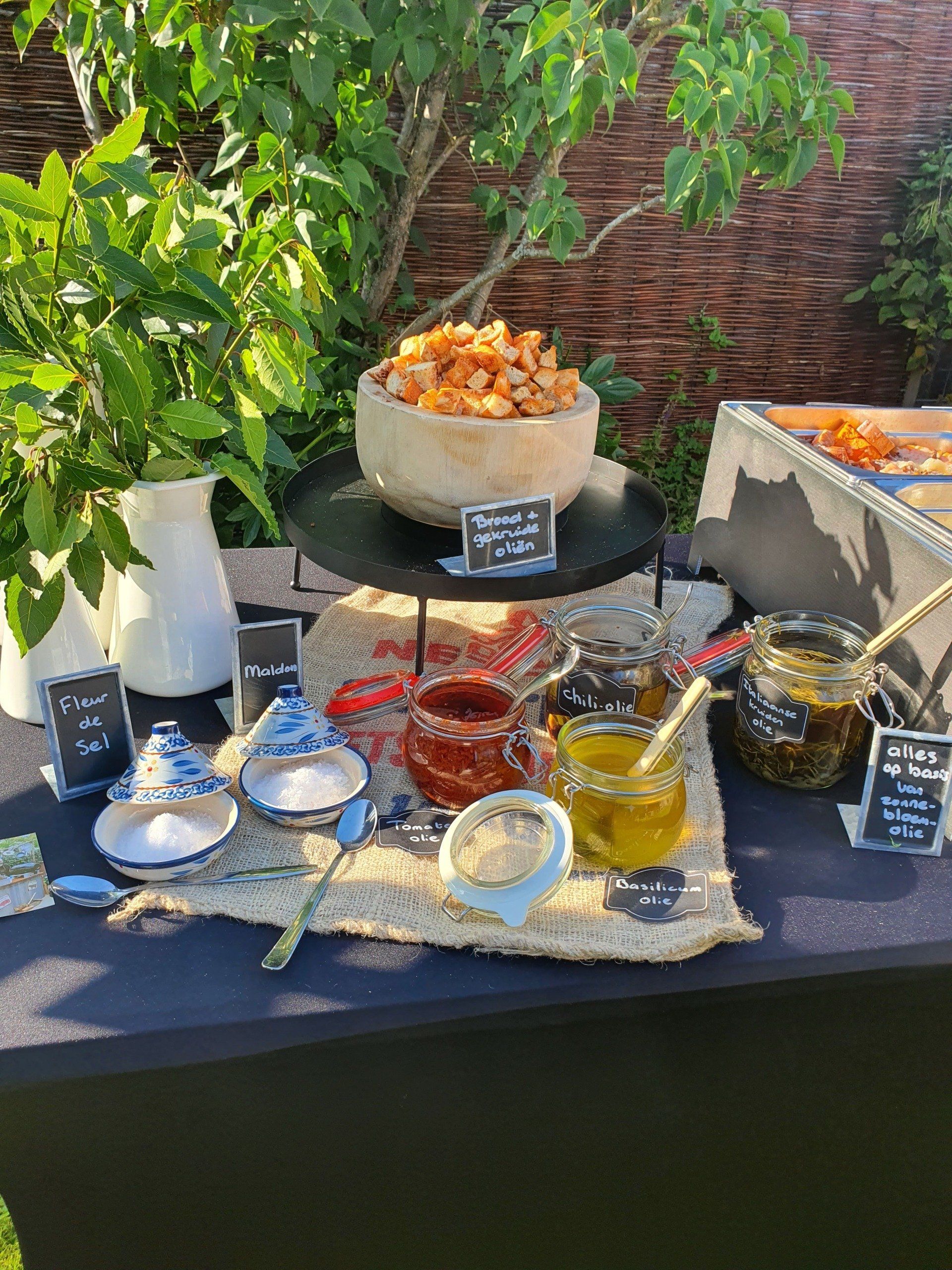 Een tafel vol hapjes buiten met dipsauzen, garnituren en een schaal met croutons op een dienblad.